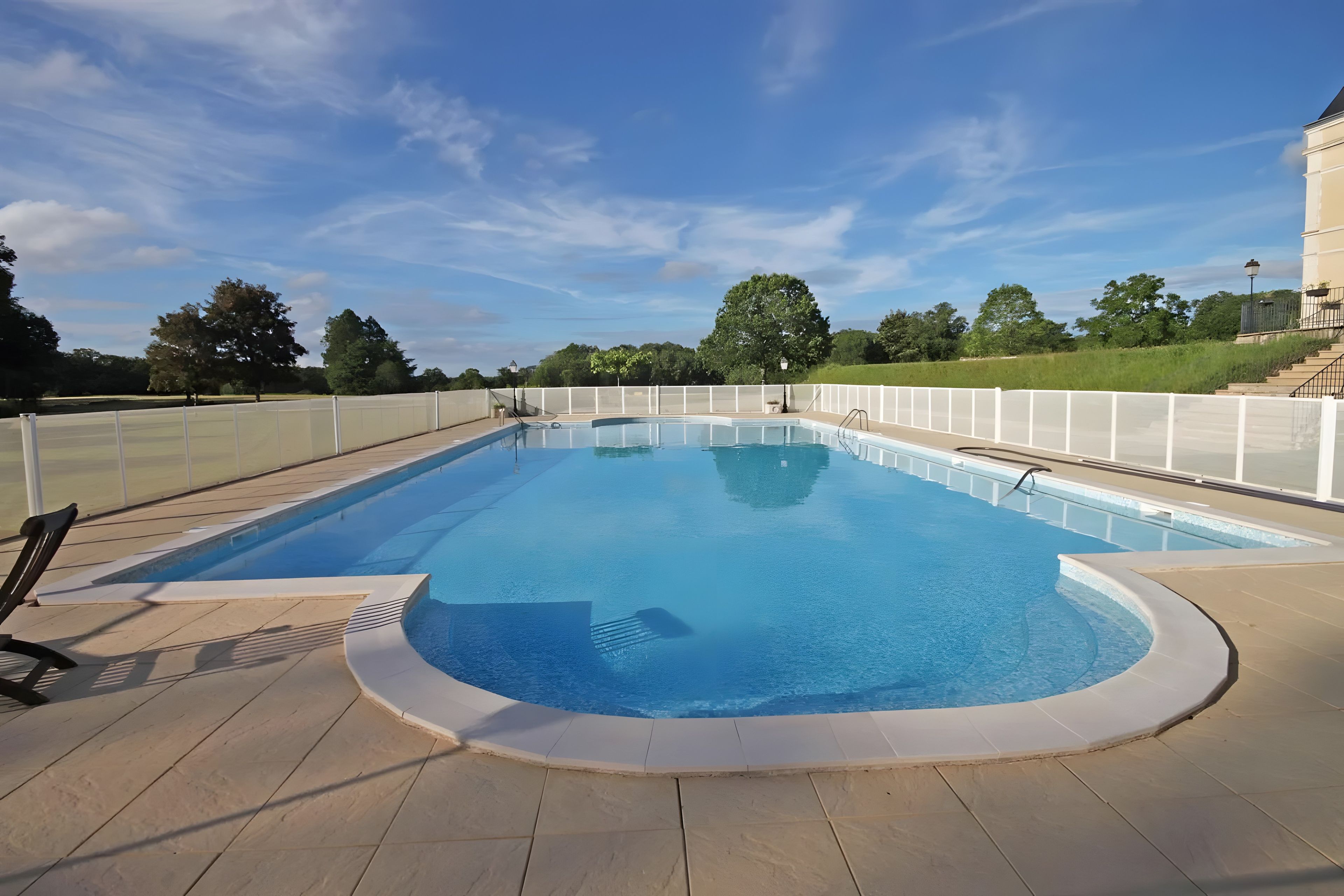 A rectangular swimming pool with a white deck and a white fence surrounding it.