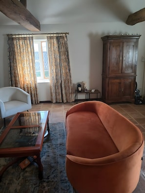 A living room with a white armchair, an orange sofa, a glass coffee table, and a wooden cabinet.