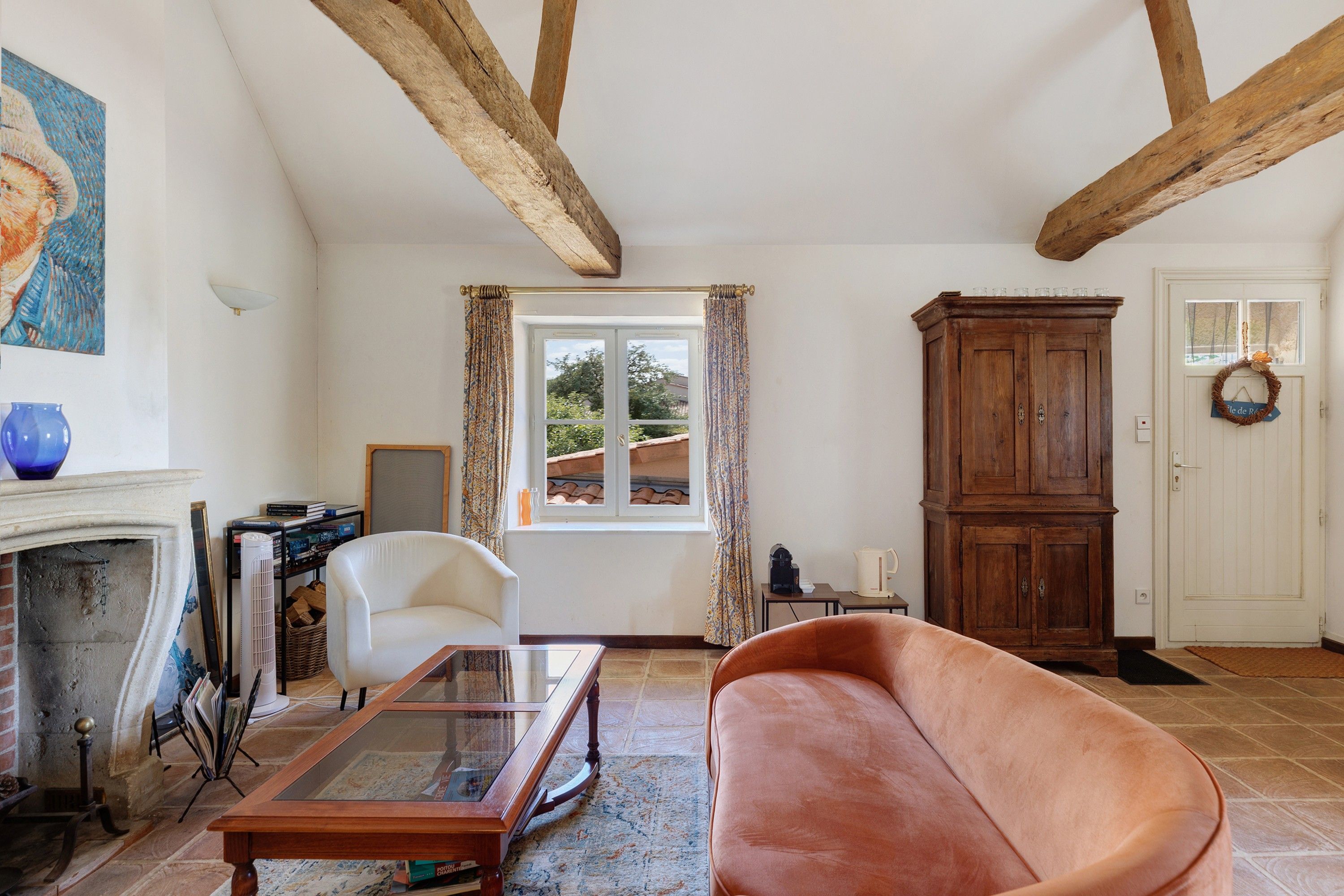 Un salon avec une cheminée, un fauteuil blanc, une table basse en verre et un meuble en bois.