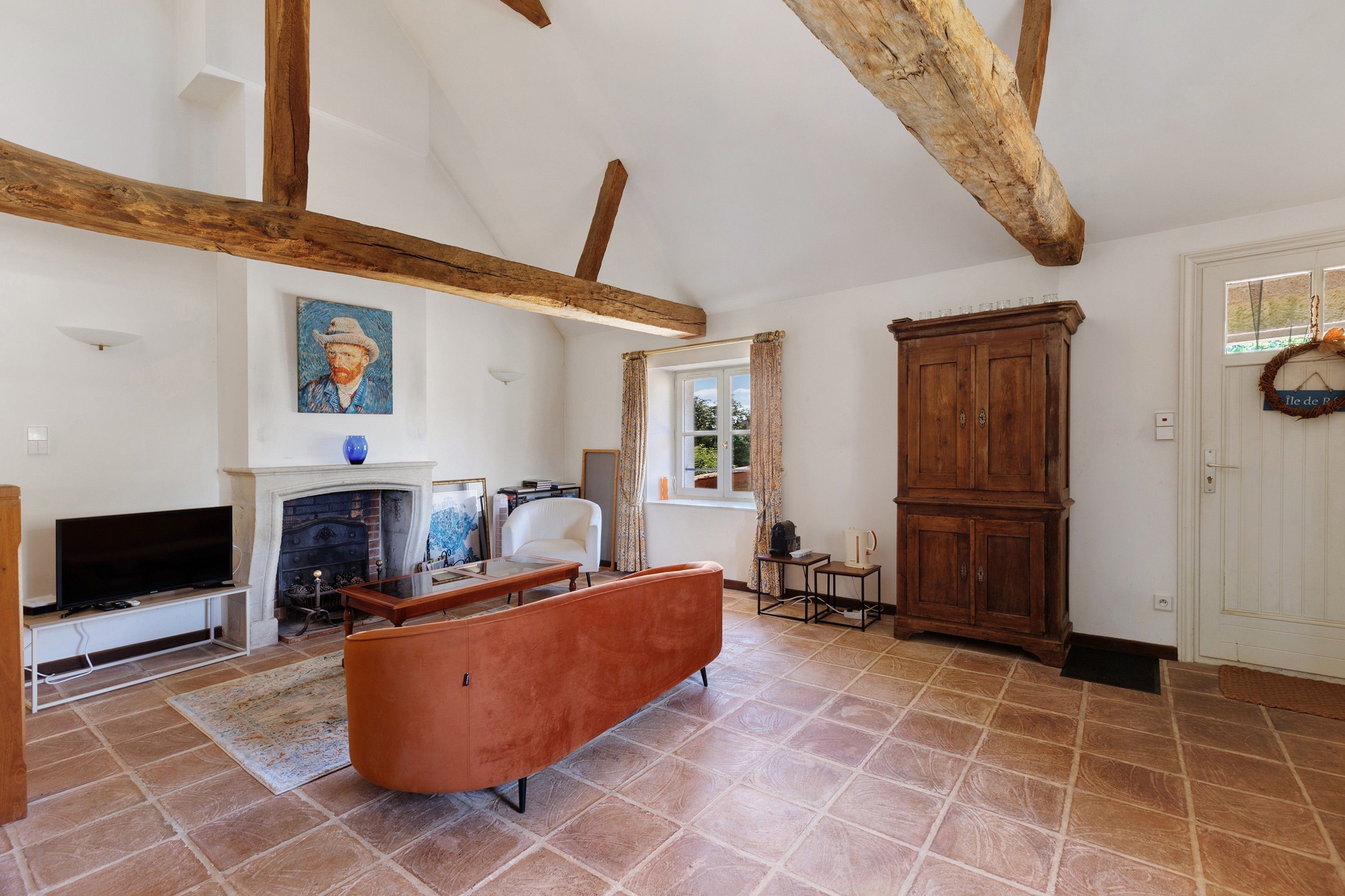 A spacious living room with exposed wooden beams, a fireplace, a television, and a large cabinet.