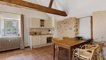 Une cuisine avec une table en bois, des chaises en osier et un mur en pierre.
