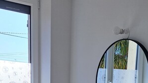 A bathroom with a wooden vanity, a round mirror, and a window with a view of palm trees.