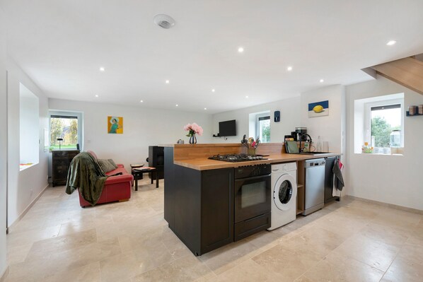 A modern kitchen with a central island, built-in oven, dishwasher, and a flat-screen TV mounted on the wall.