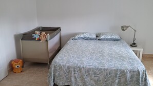 A bedroom with a bed, a nightstand, a lamp, a crib, and a teddy bear.