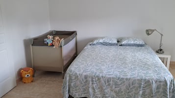 A bedroom with a bed, a nightstand, a lamp, a crib, and a teddy bear.