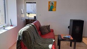 A living room with a red sofa, a blanket, a small table with a remote control, and a painting on the wall.