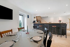 A dining area with a table set for four, a kitchen in the background, and a staircase leading to an upper level.