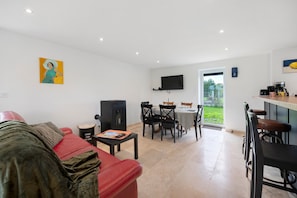 A modern living room with a red sofa, a flat-screen TV mounted on the wall, and a dining area with a table and chairs.