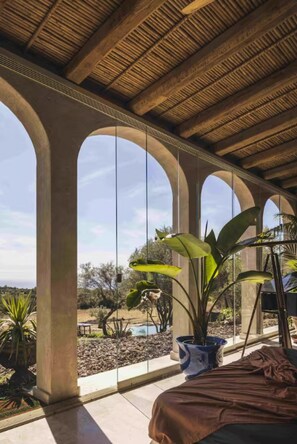 Ein Zimmer mit hohen Decken, großen Bogenfenstern und Blick ins Freie.