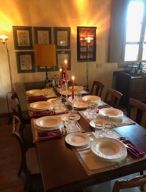 Ein Esstisch, gedeckt für eine Mahlzeit, mit Kerzen, gerahmten Bildern an den Wänden und einem Fenster im Hintergrund.