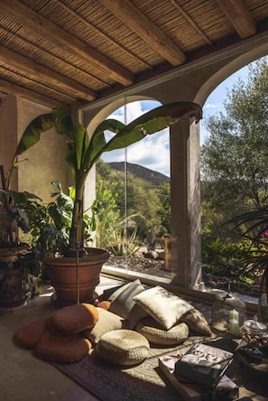A room with a thatched ceiling, a large potted plant, and a view of a mountainous landscape through a glass door. - The Olive Grove – Luxury Country Resort with Panoramic Views and Private SPA in Sardinia (Quartu Sant'Elena)