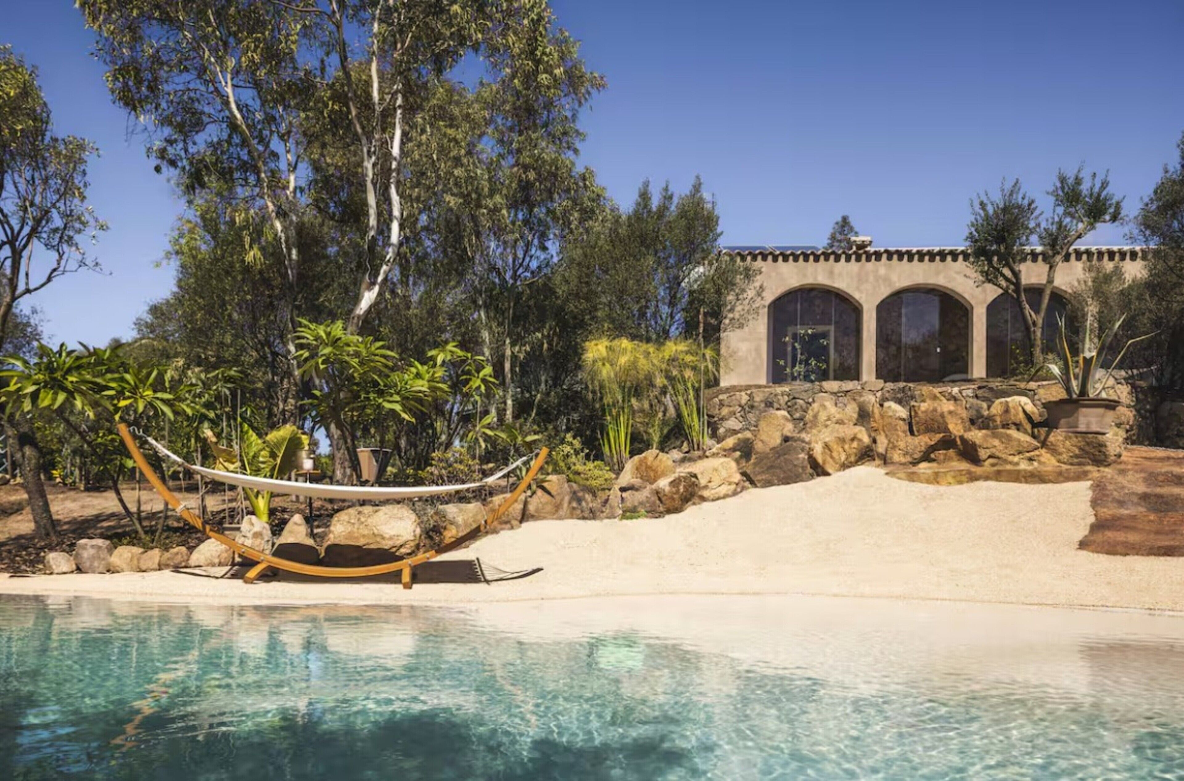 Una piscina con agua cristalina, rodeada de rocas y una hamaca.