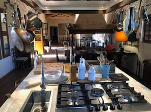 A modern kitchen with stainless steel appliances, hanging pots, and a central island with a sink and stove. - The Olive Grove – Luxury Country Resort with Panoramic Views and Private SPA in Sardinia (Quartu Sant'Elena)