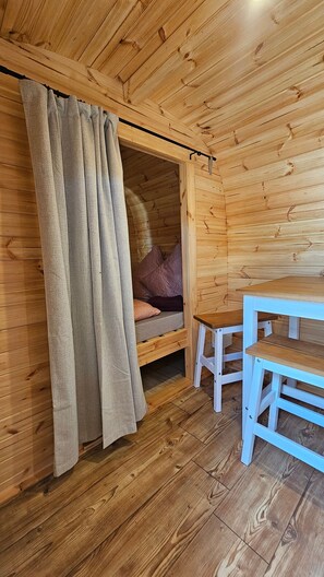 A wooden cabin interior with a bed, a table, and a curtain.