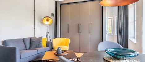 Uma sala de estar moderna com um sofá cinzento, uma poltrona amarela, uma mesa de centro redonda e um abajur.