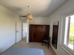 Ein Schlafzimmer mit Bett, Kleiderschrank, Sessel, Pendelleuchte und Fenster.