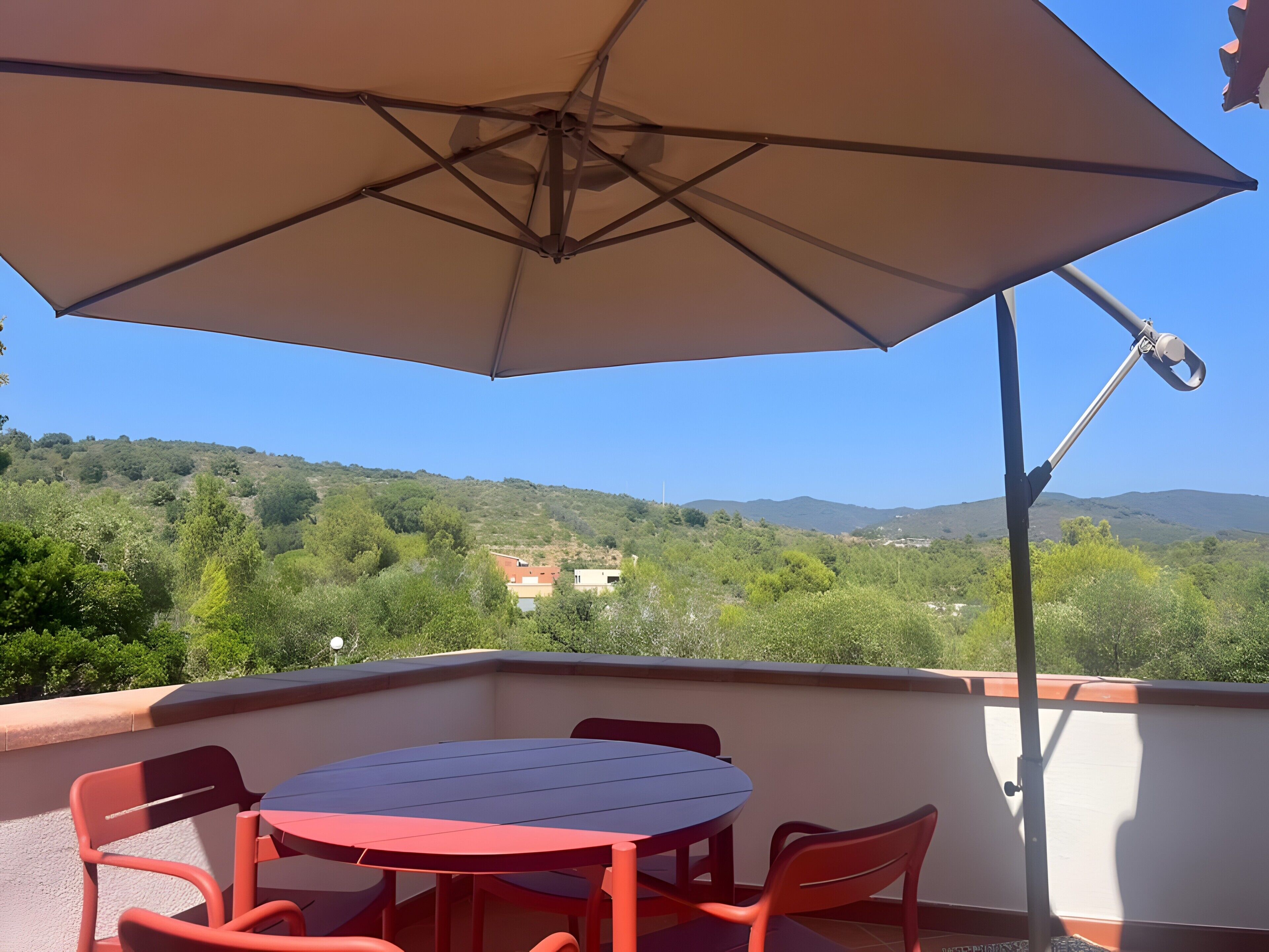 A balcony with a round table and chairs, an umbrella, and a view of a hilly landscape.