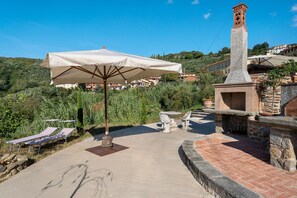 Un patio con una gran sombrilla, mobiliario exterior y una estructura de piedra con una torre de reloj.