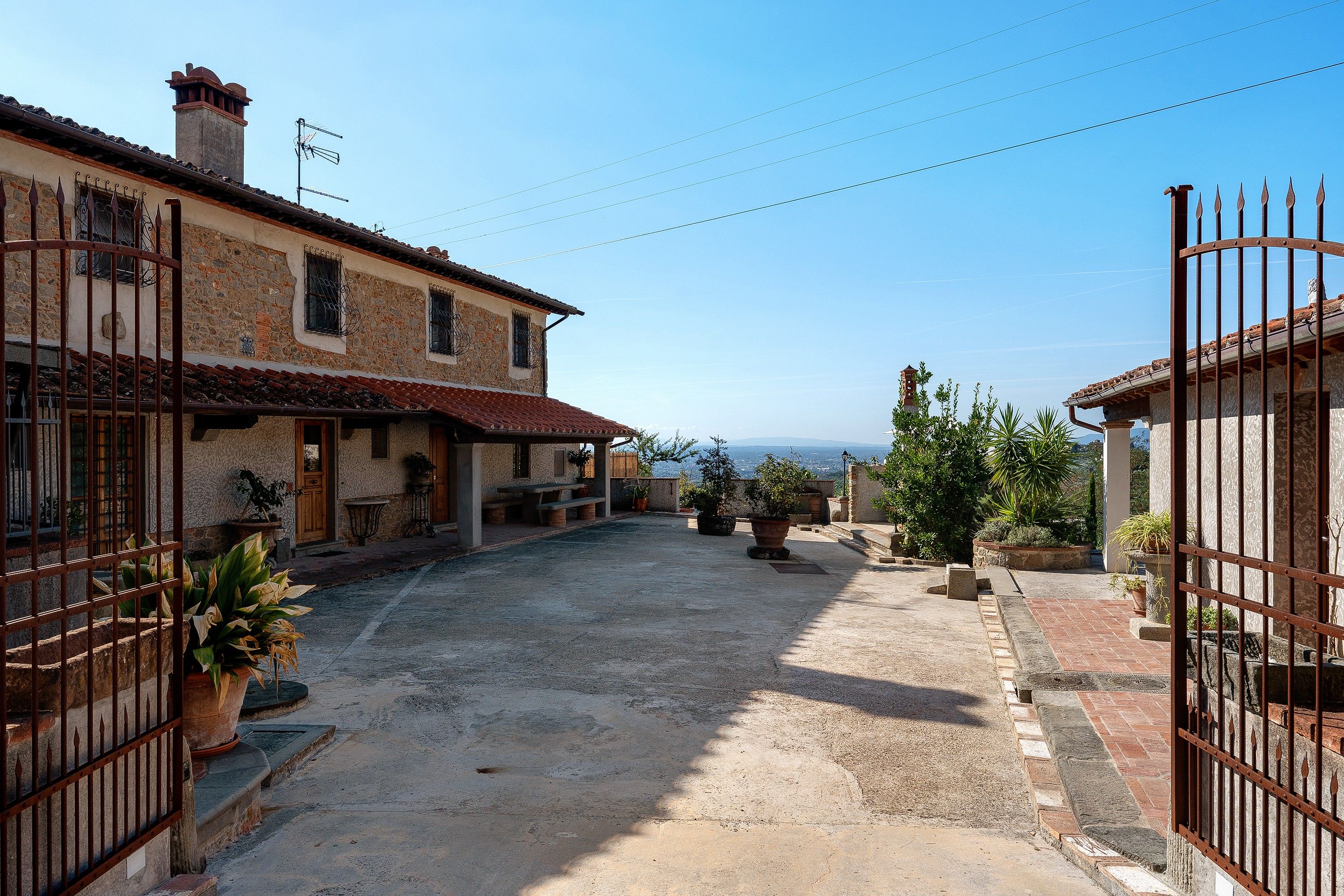 Un cortile con edifici in pietra, un cancello e piante in vaso.