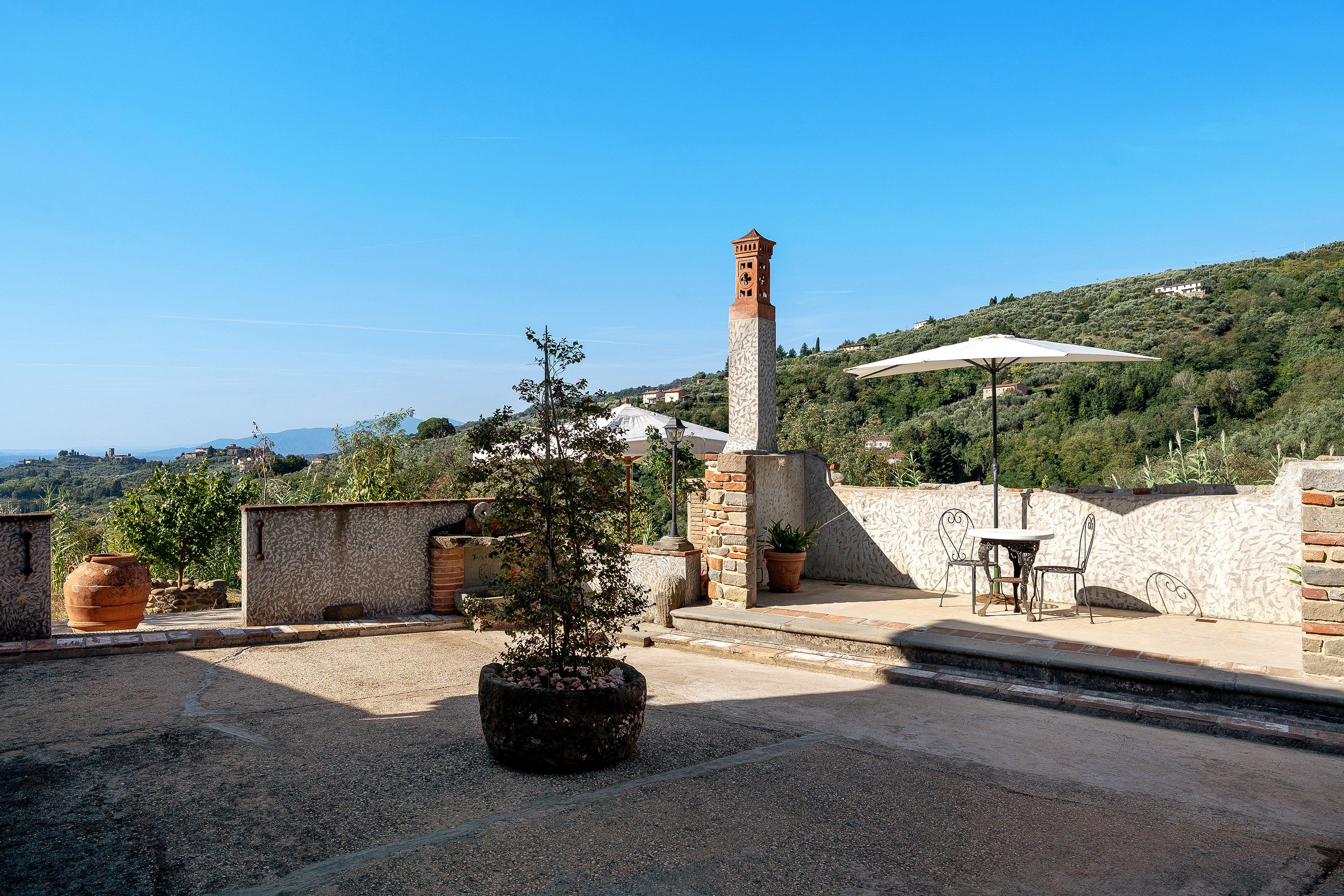 Une terrasse sur le toit, agrémentée d’un clocher en pierre, de plantes en pot et d’une table avec des chaises.