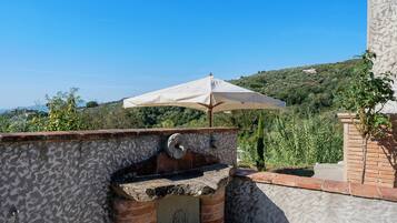 Eine Dachterrasse mit einem Backofen, einem Sonnenschirm und Blick auf eine hügelige Landschaft.