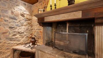 A stone fireplace with a metal grate, a wooden mantelpiece, and a stone wall with a textured finish.