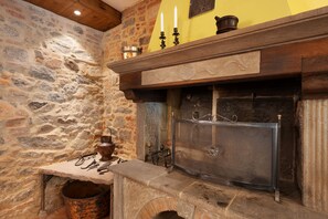 A stone fireplace with a metal grate, a wooden mantelpiece, and a stone wall with a textured finish. - Podere del Convento – House with Garden and Tuscan Views (Massa e Cozzile)