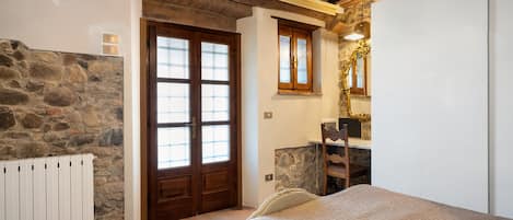 A bedroom with a stone wall, wooden door, and a bed with a quilted cover.