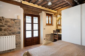 A bedroom with a stone wall, wooden door, and a bed with a quilted cover.