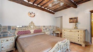 A bedroom with a stone wall, a bed with ornate headboard, a dresser, and a chandelier.