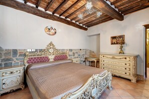 Ein Schlafzimmer mit Steinwand, einem Bett mit aufwendigem Kopfteil, einem Schminktisch und einer Kandelaber.