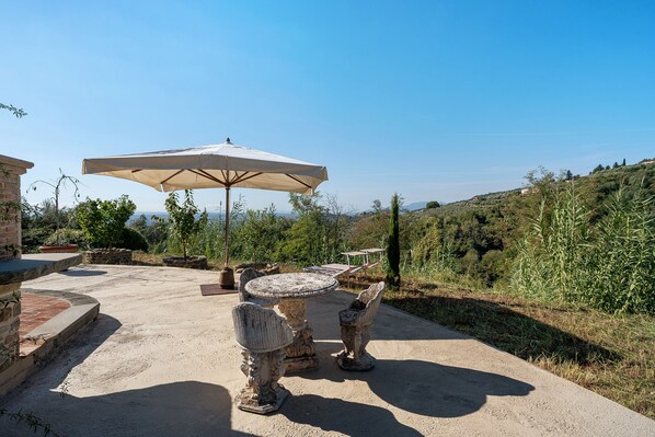 An outdoor patio with a table and chairs, an umbrella, and a view of the surrounding landscape.