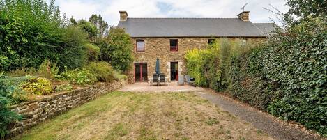 Une maison en pierre avec une allée en gravier, un petit patio agrémenté de meubles d’extérieur et un jardin bien entretenu.