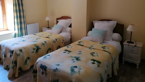 A hotel room with two beds, each with a floral bedspread, bedside tables with lamps, and a window with curtains.