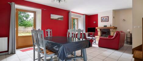 A dining area with a table and chairs, a red sofa, a fireplace, and a television.