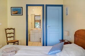 A bedroom with a bed, a chair, a nightstand, a lamp, and a view of a bathroom through an open door.