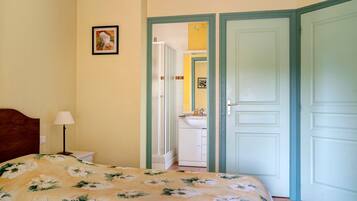 Un dormitorio con cama, mesita de noche, lámpara, puerta y baño a la vista a través de una puerta abierta.