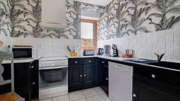 A kitchen with black and white patterned wallpaper, white tiled walls, a microwave, stove, and a sink.