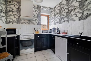 A kitchen with black and white patterned wallpaper, white tiled walls, a microwave, stove, and a sink.