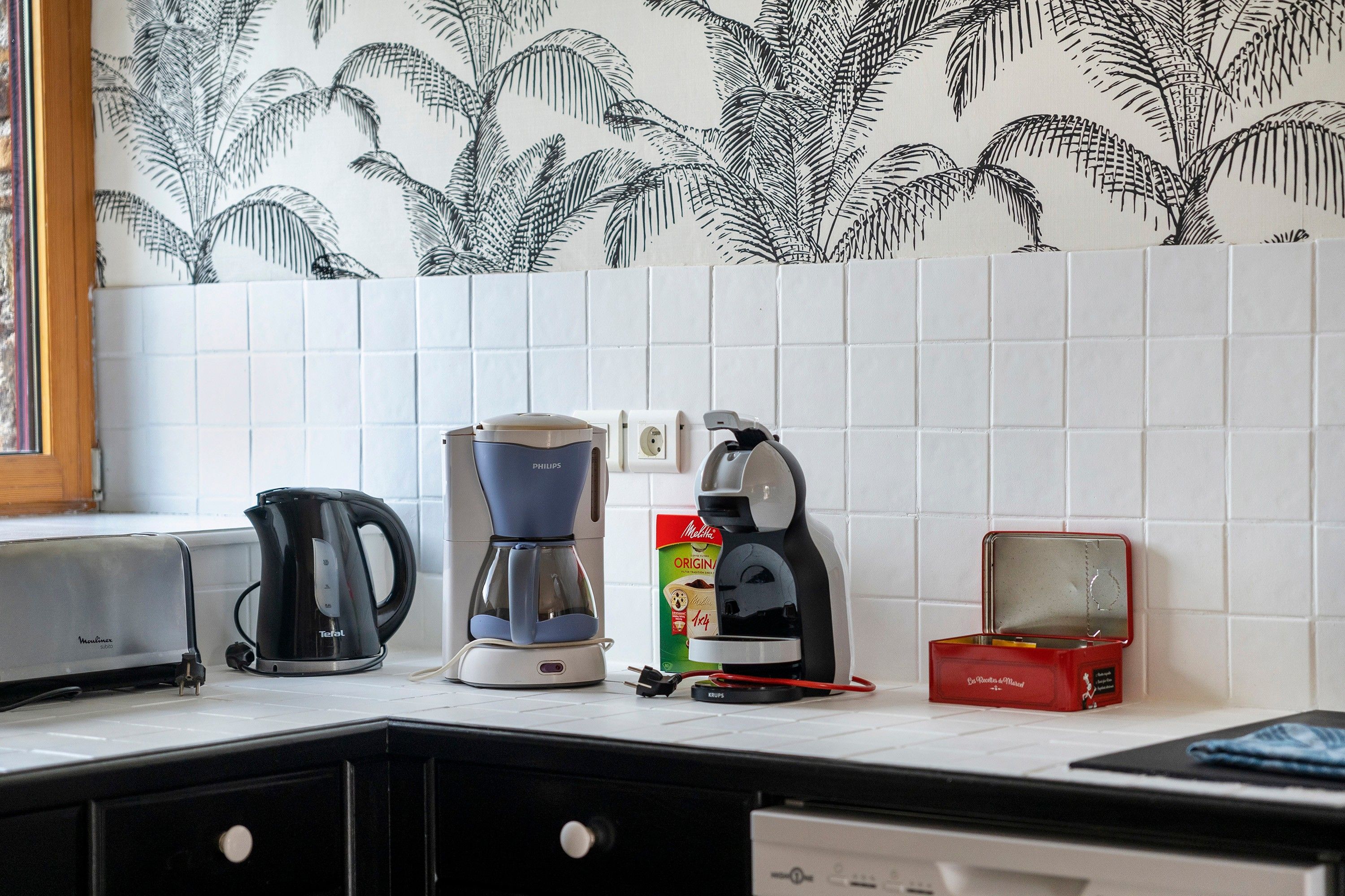Una cocina con cafetera, hervidor y una caja de cápsulas de café sobre la encimera.