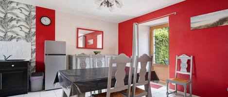 Een eethoek met een tafel, stoelen, een koelkast, een klok en een raam met uitzicht.