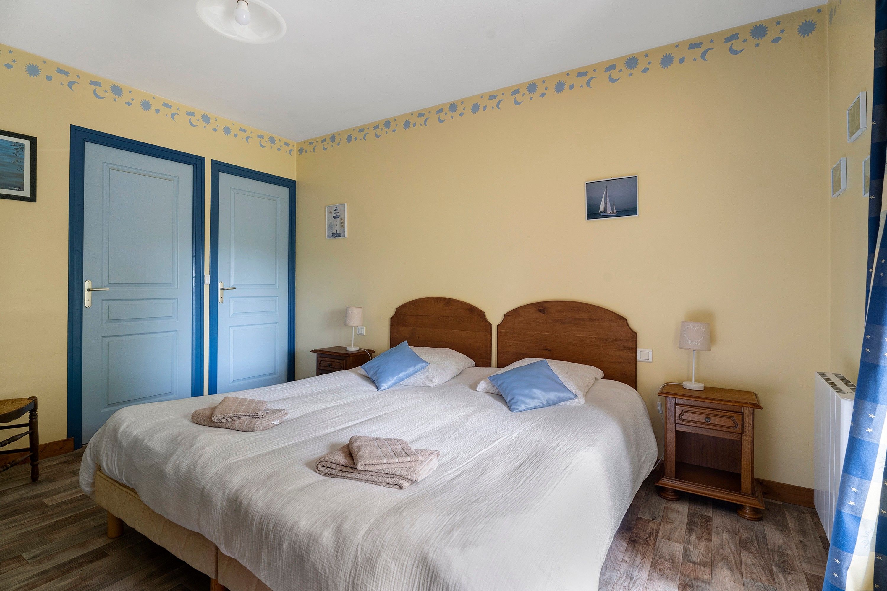 Une chambre à coucher avec un lit double, deux tables de chevet avec des lampes, une tête de lit en bois et un mur orné d’un motif décoratif.