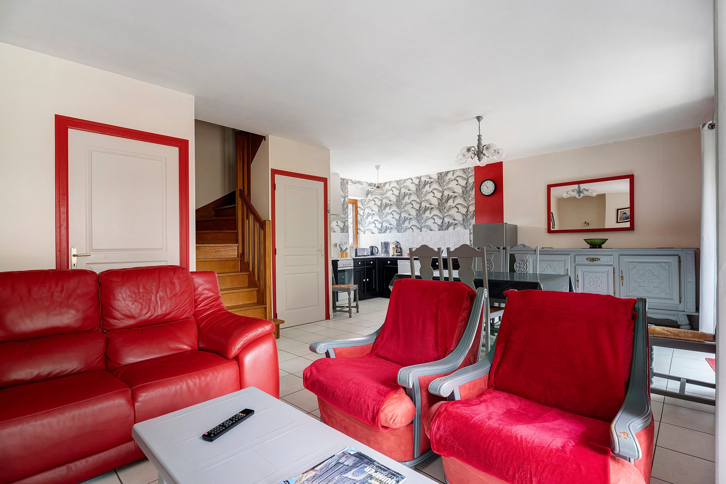 Un salon avec un canapé rouge, une table basse et un coin repas comprenant une table et des chaises.