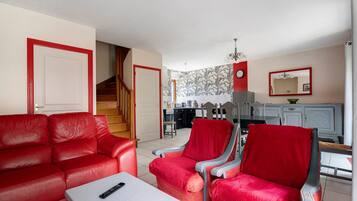 Un salon avec un canapé rouge, une table basse et un coin repas comprenant une table et des chaises.