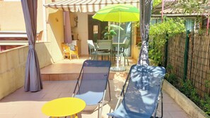 En udendørs terrasse med to liggestole, et lille gult bord og en grøn parasol.