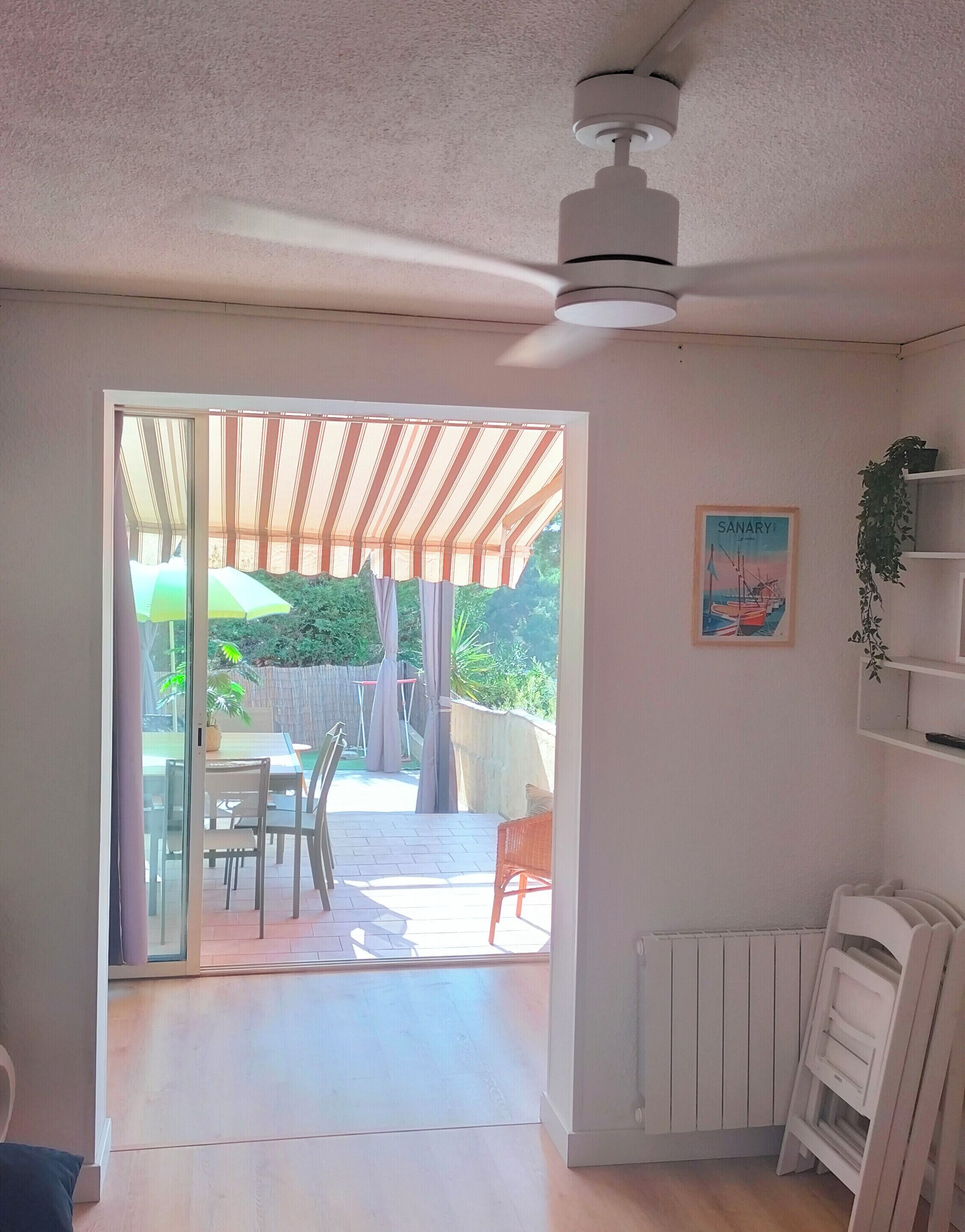 A room with a ceiling fan, a sliding glass door leading to an outdoor patio with a table and chairs, a radiator, and a framed picture on the wall.
