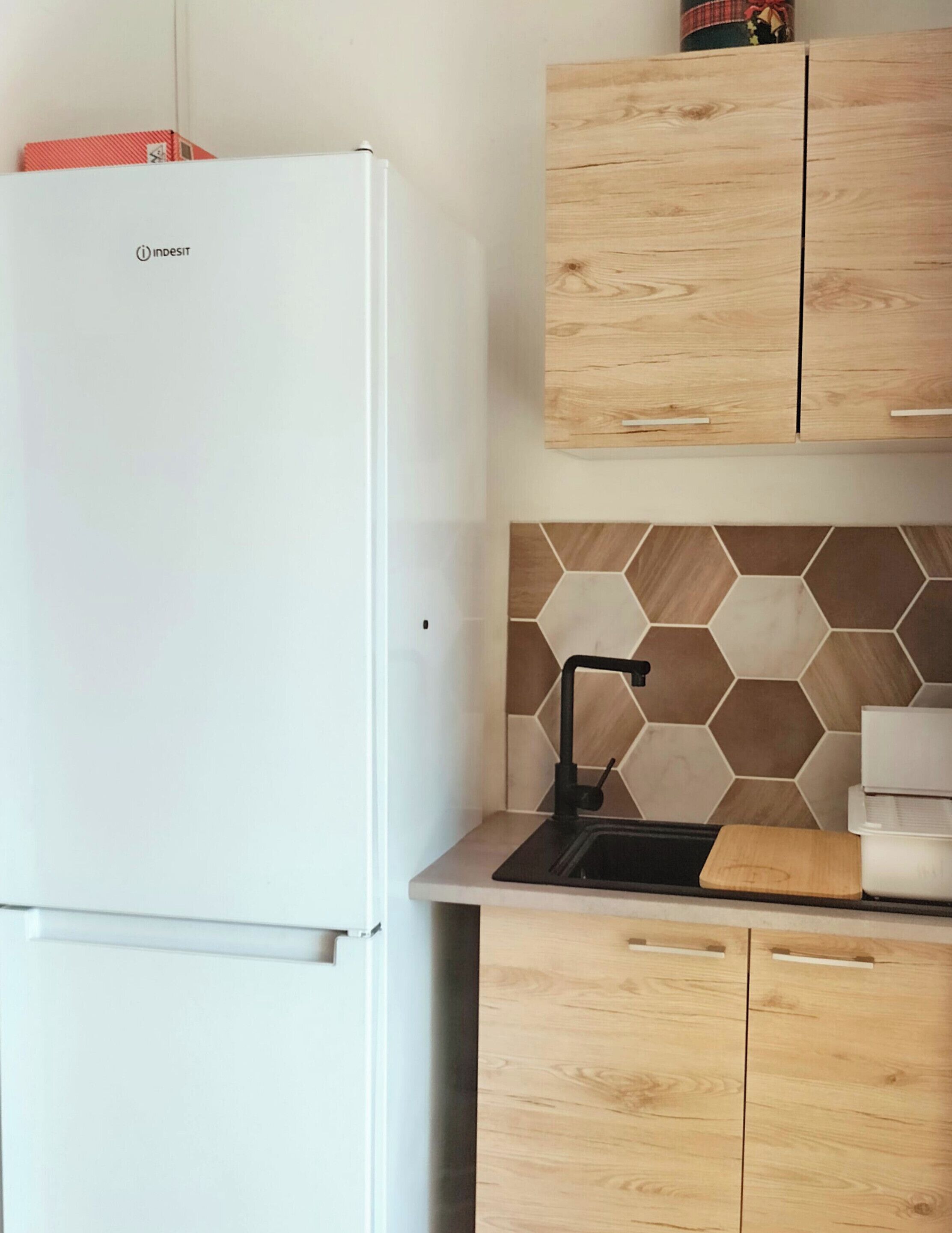 Eine Küche mit einem weißen Kühlschrank, Holzschränken, einer sechseckigen Fliesenrückwand und einem schwarzen Wasserhahn.