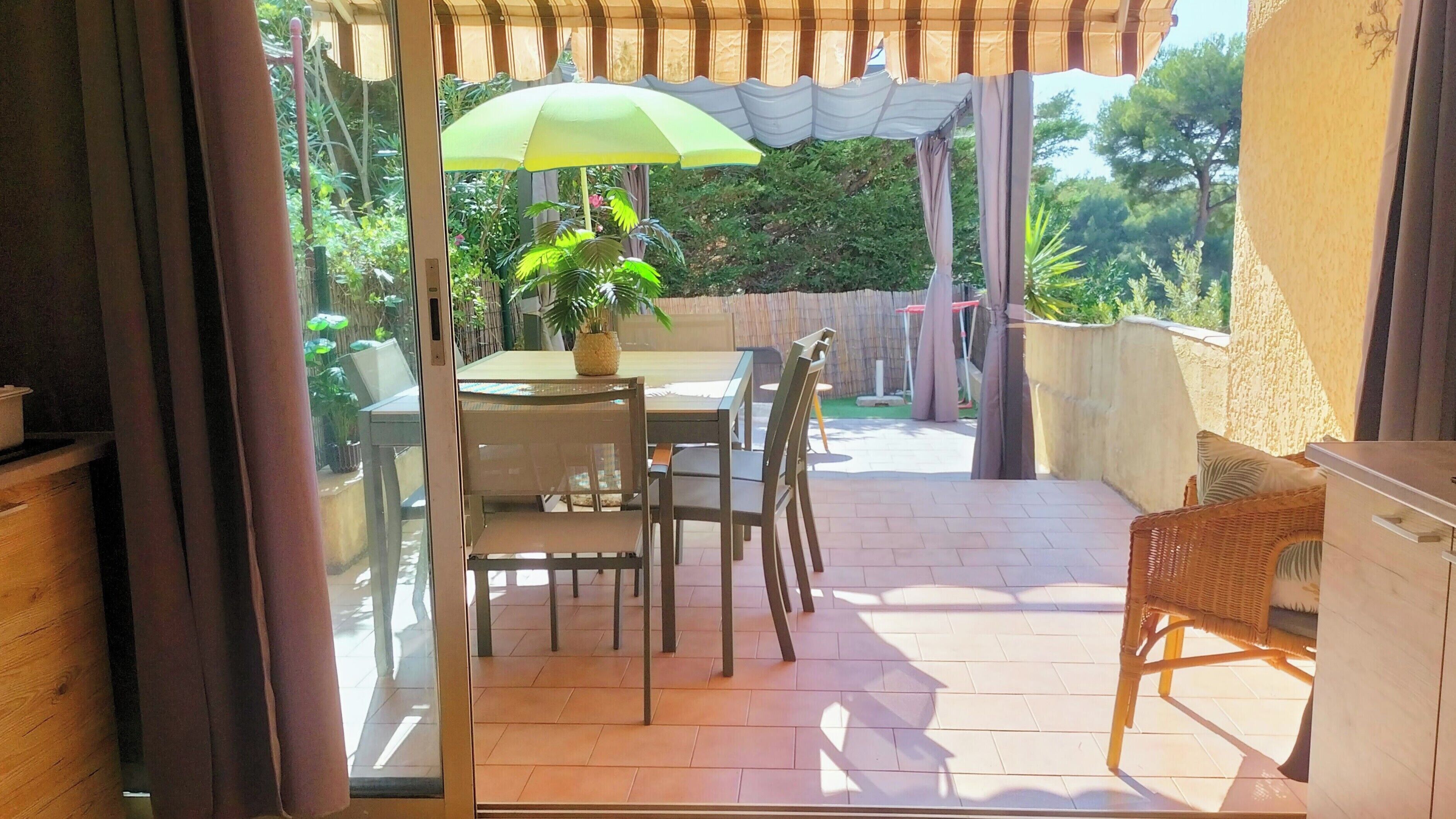 Un patio exterior con una mesa y sillas, una planta en maceta y una pérgola con toldo.
