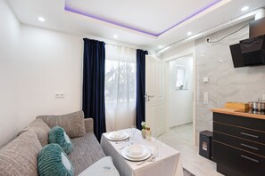 Ein modernes Wohnzimmer mit einer Couch, einem Esstisch für zwei Personen und einer Küchenzeile inklusive Fernseher und Mikrowelle.