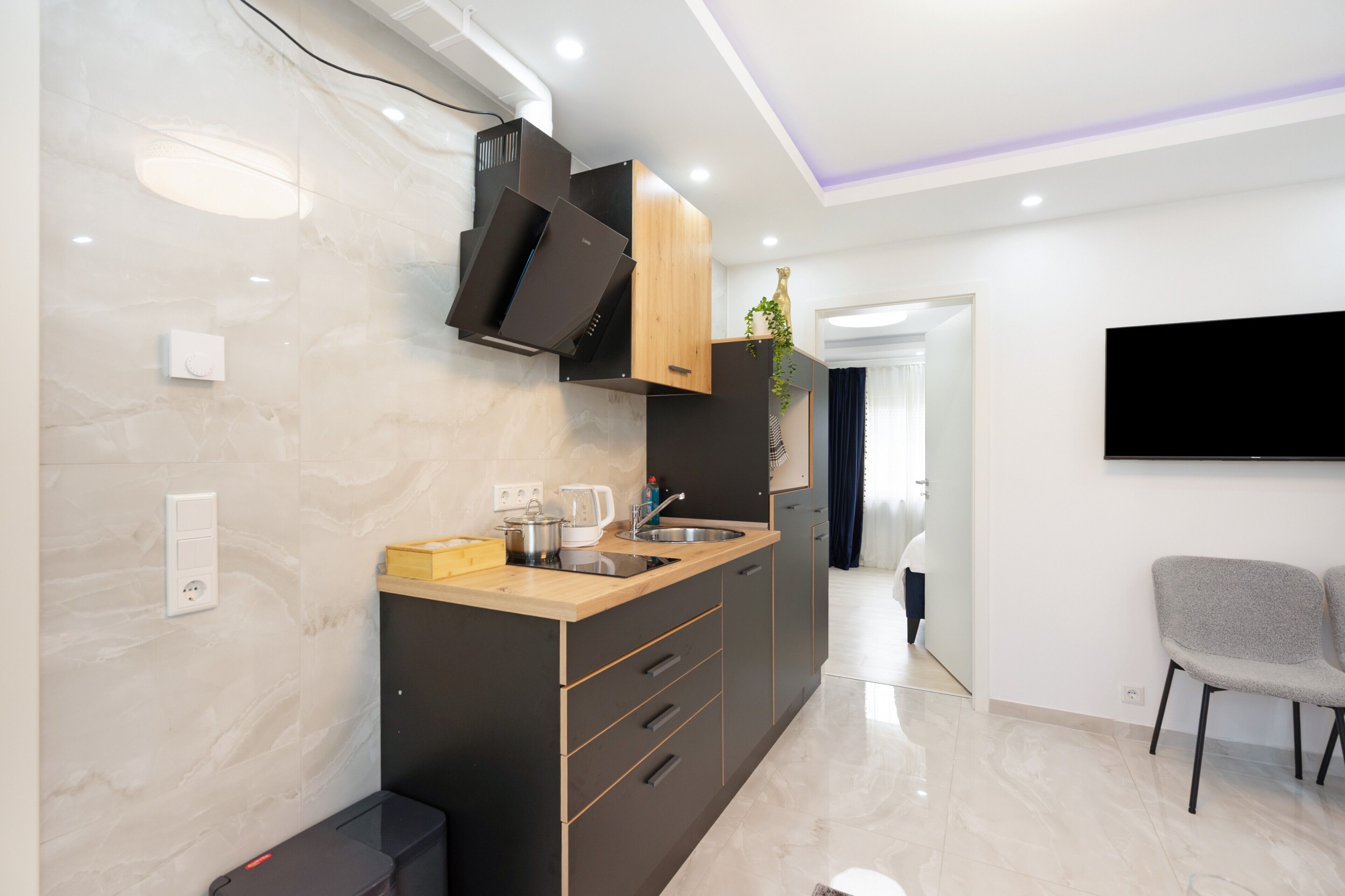 Eine moderne Küche mit Einbauherd, Spüle und Holzarbeitsplatte. An der Wand ist ein Fernseher befestigt und im angrenzenden Wohnbereich steht ein Sessel.